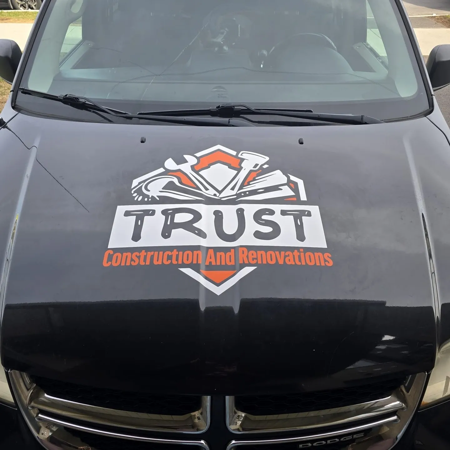 Cut vinyl TRUST Construction and Renovations logo applied to the hood of a black minivan