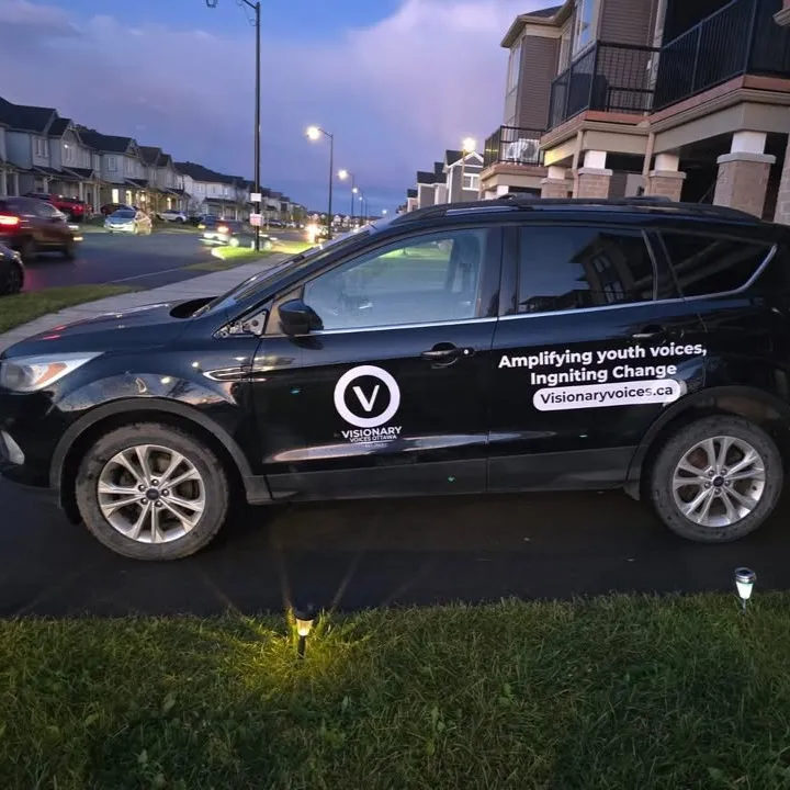 Black SUV with white Visionary Voices roundel on the front door and tagline lettering along the rear door